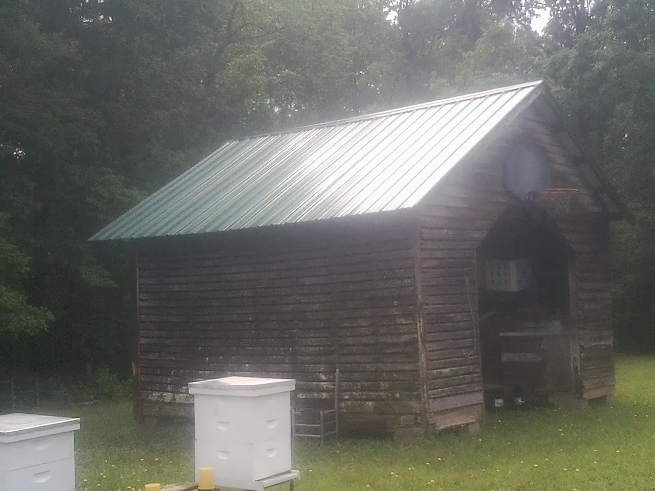 Green metal roof on a weathered barn beside stacked beehives in Weatogue