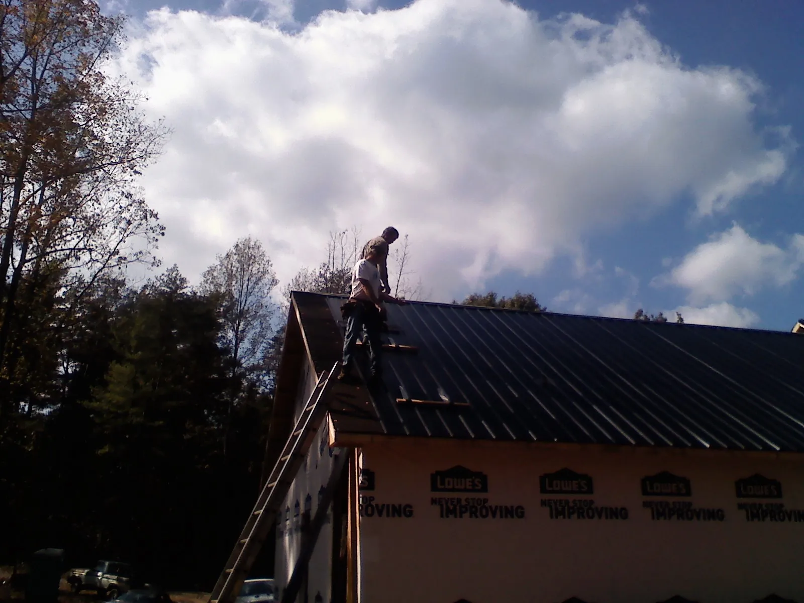 Roofer fastening dark metal panels high against a cloudy sky, from a Roof Inspection job in Weatogue