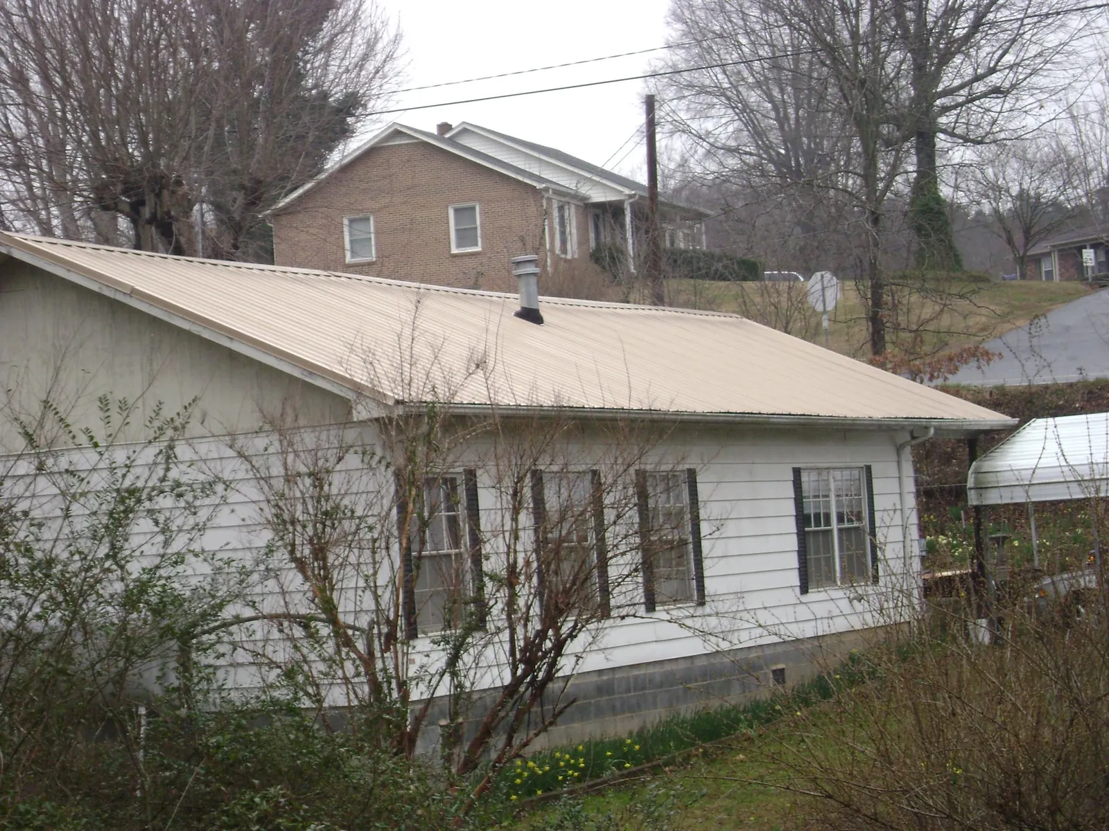 Tan metal roof on a white sided house set into a hillside — Commercial Roofing by Roofing Brothers in Weatogue